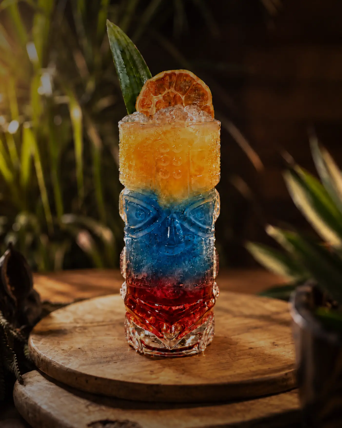 Layered orange, blue and red cocktail in a carved glass with charred lime
