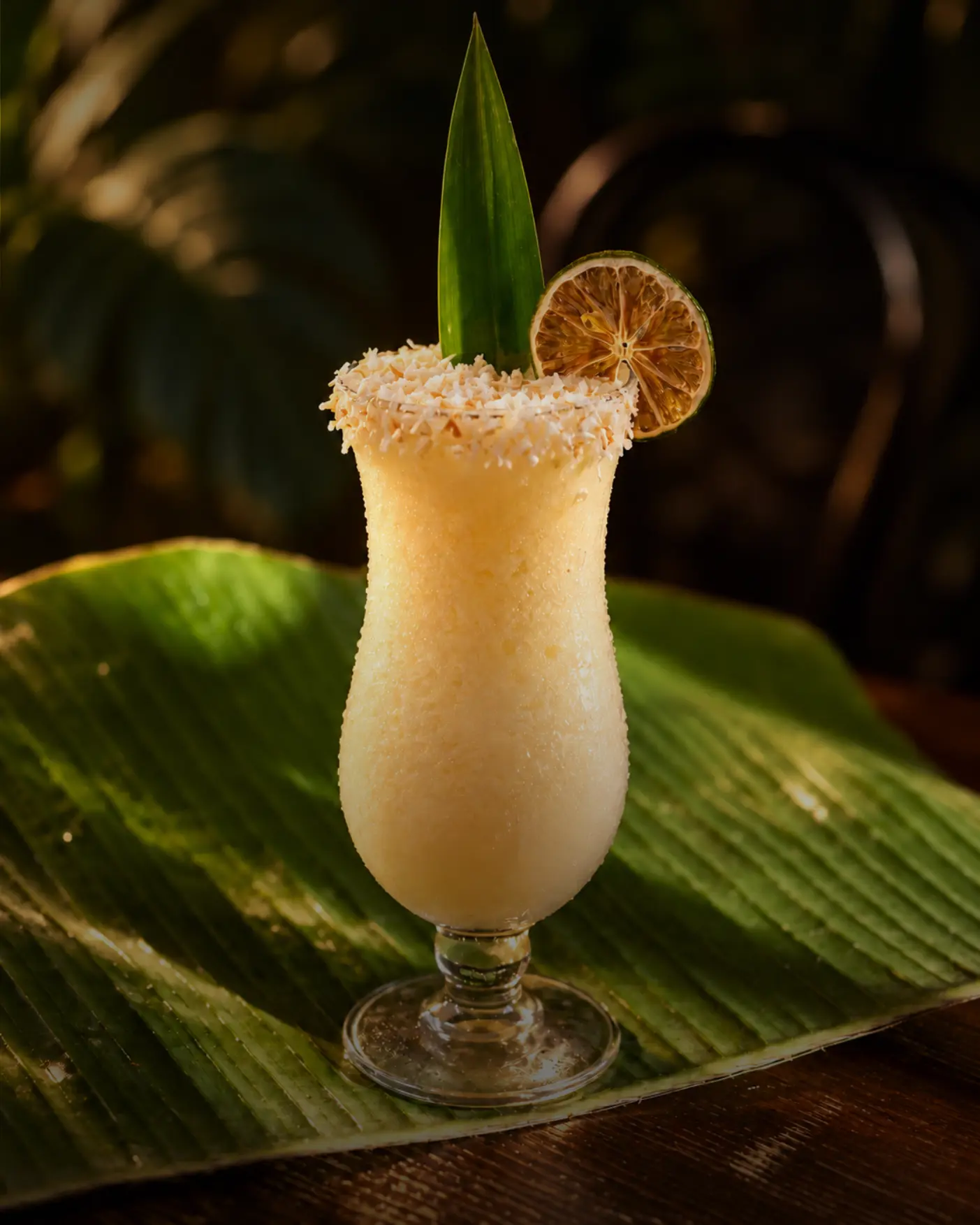 Creamy coconut cocktail with a toasted coconut rim and dried lime on a banana leaf